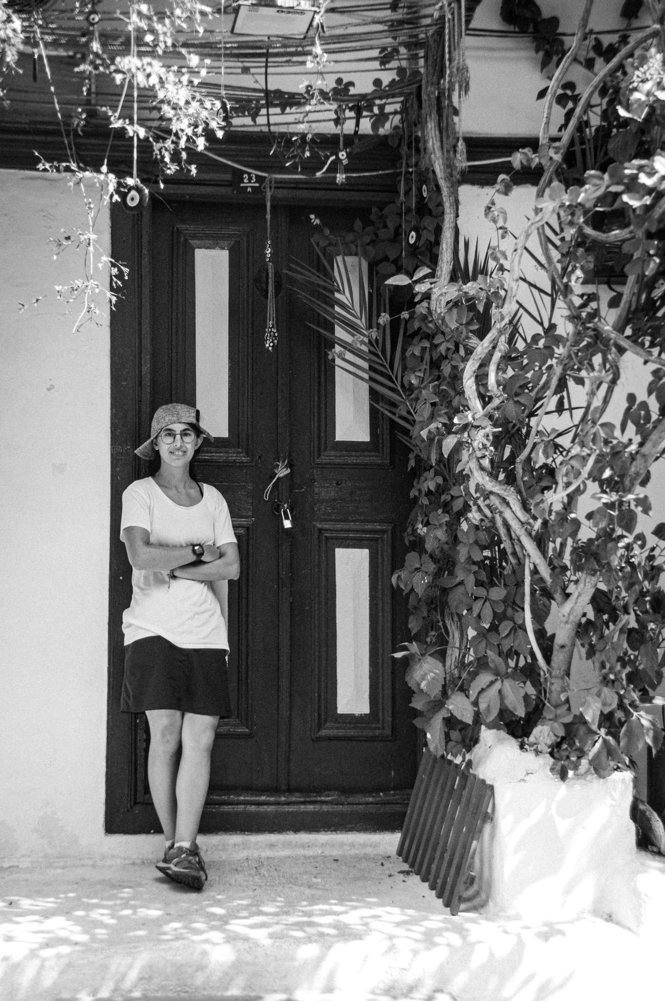 Person standing by a rustic door surrounded by plants, in black and white.