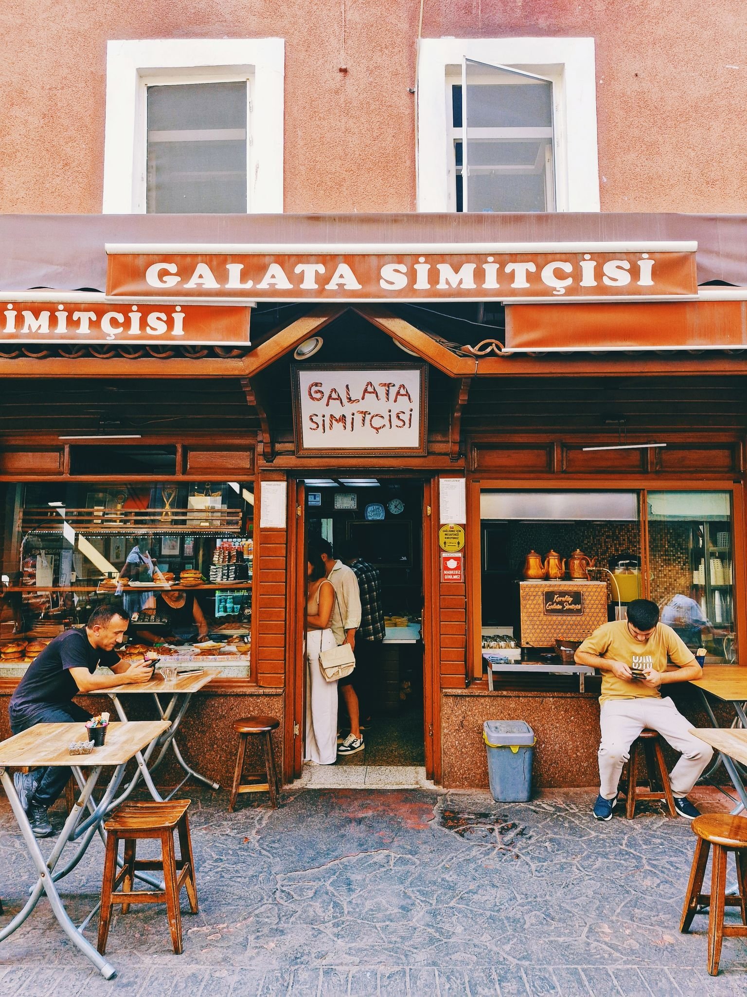 Two people sitting outside the Galata Simitçisi in Istanbul, enjoying traditional Turkish simits.