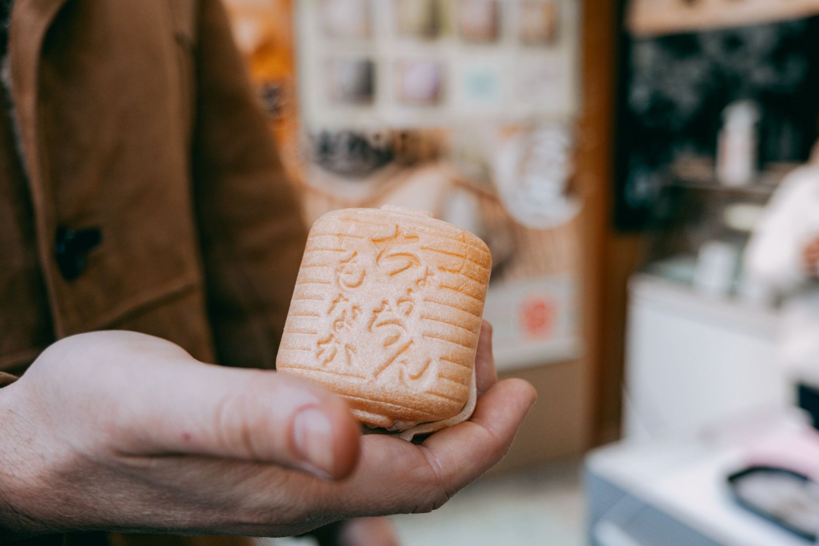 Hand holding traditional Japanese monaka sweet in Tokyo shop setting.