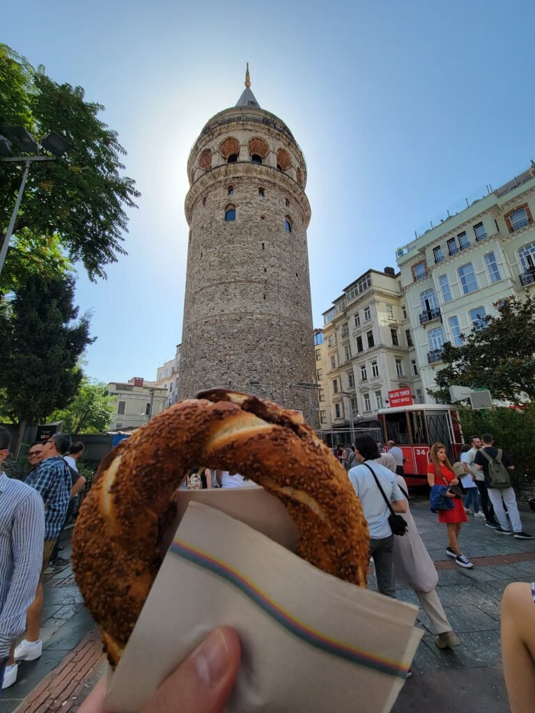 Simit held up in front of Galata Tower and a red tram in Istanbul